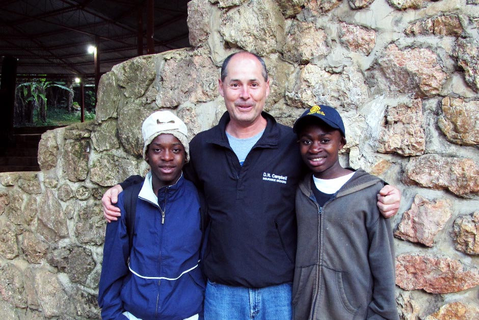 Volunteer with two boys in front of a stone wall